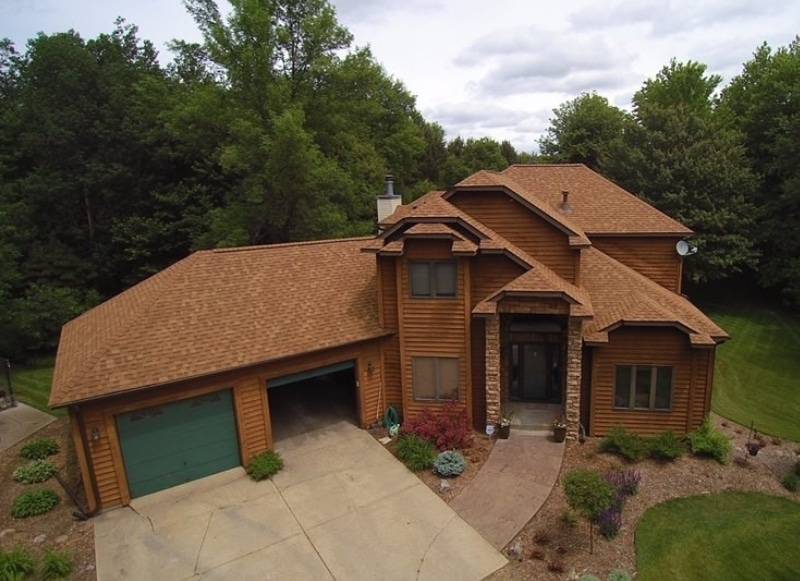 Aerial view of a residential home with brown asphalt shingle roofing and wood siding